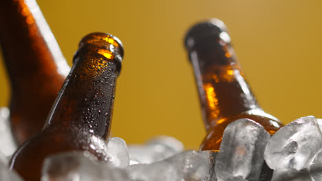 Cerca-De-Botellas-De-Vidrio-De-Cerveza-Fría-O-Refrescos-Enfriándose-En-Un-Cubo-Lleno-De-Hielo-Contra-Fondo-Amarillo